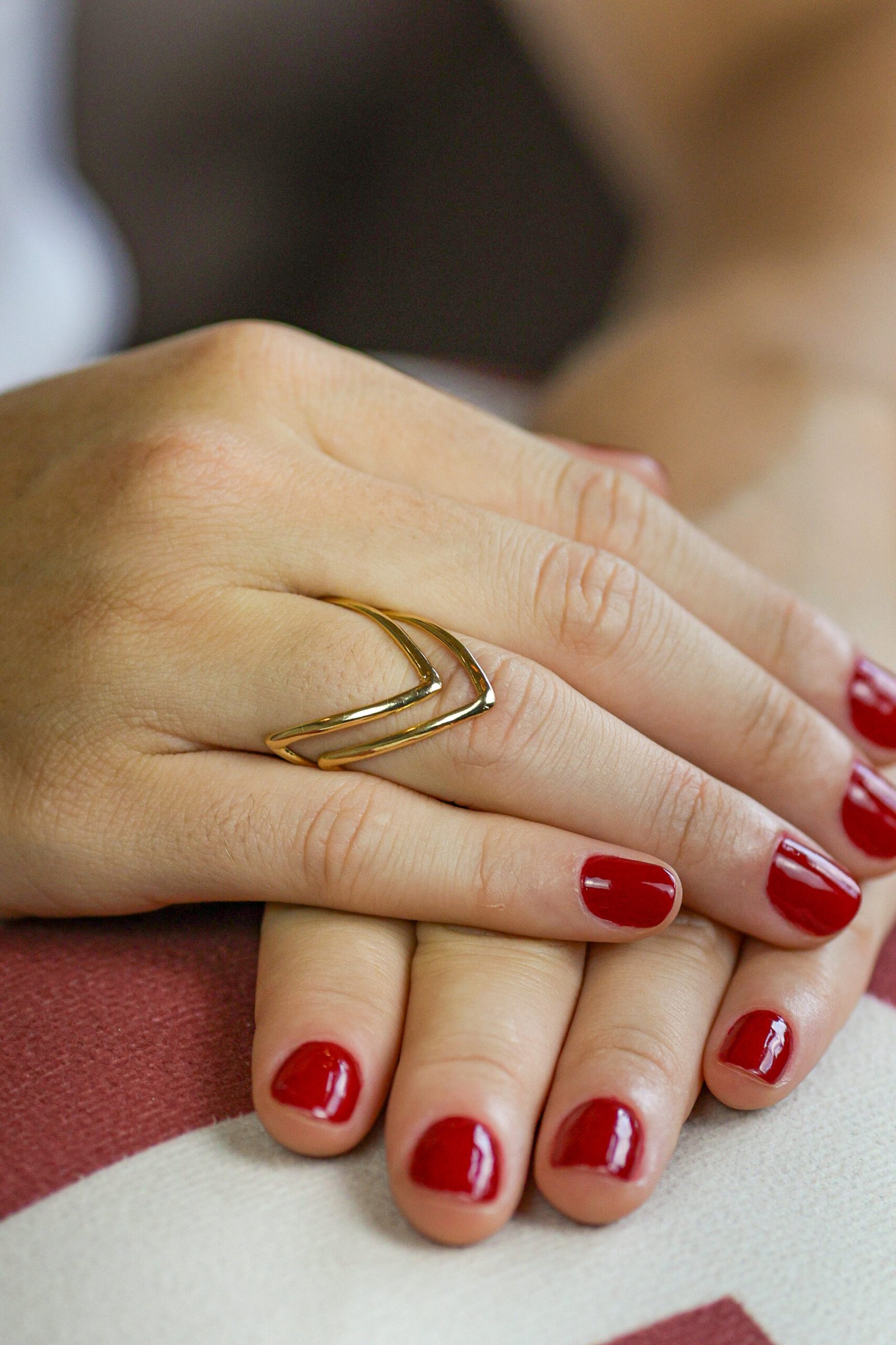 Mão com anel aro geométrico em V liso, destaque para anéis folheado a ouro banhado, unhas vermelhas.
